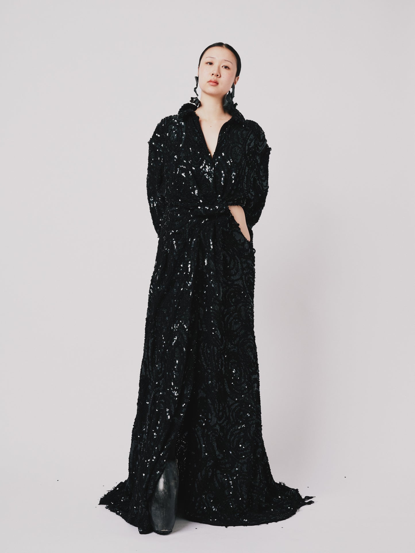 Woman wearing a black sequin Marq twisted draped dress against a white background. Front view