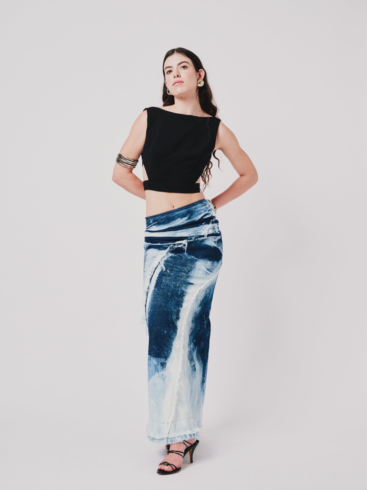 Woman wearing a black top and structured drape skirt in blue denim on a white background. Font view