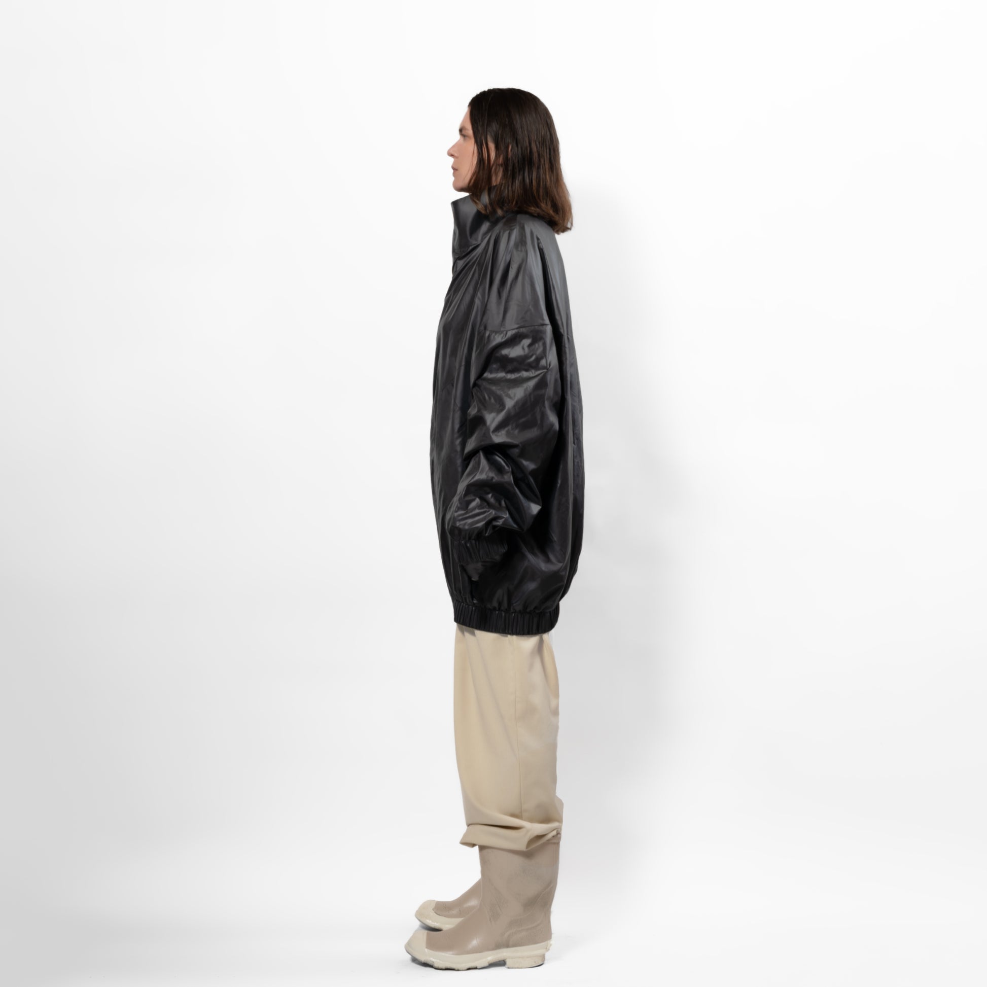 Black 90's inspired windbreaker Jacket with slight Sheen. Front zip, elasticated bottom hem and cuff. long front zip. one size fits all. Side view.