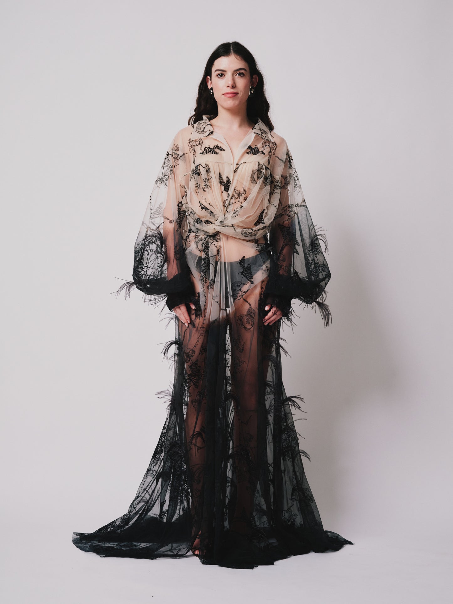 Woman wearing a sheer black and nude outfit with embroider patterns on a white background