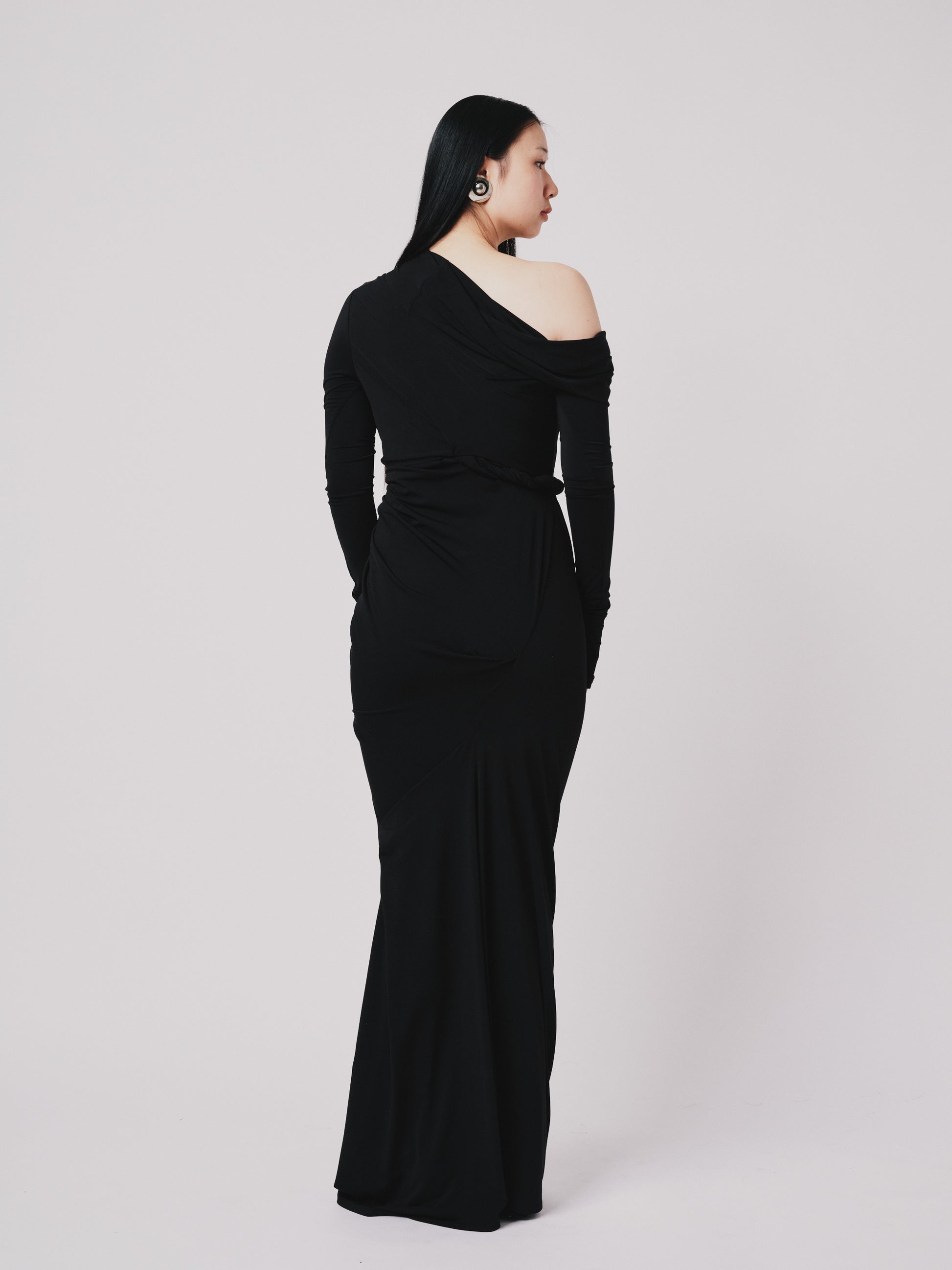 Woman wearing a black off-shoulder gown on a white background back view 