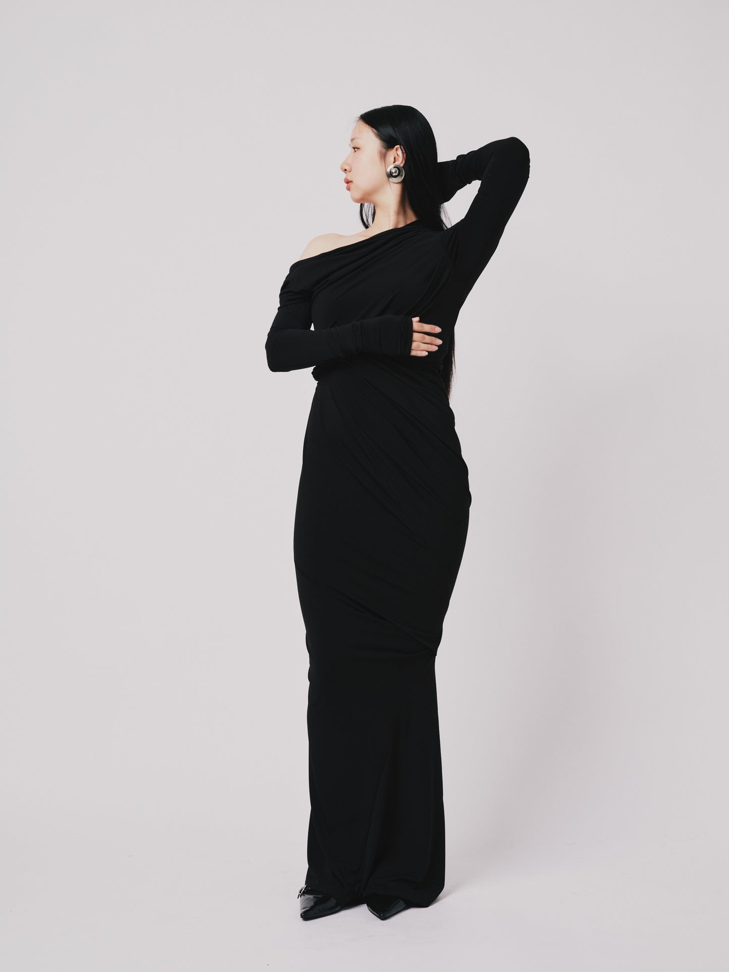 Woman wearing a black off-shoulder dress against a white background posing