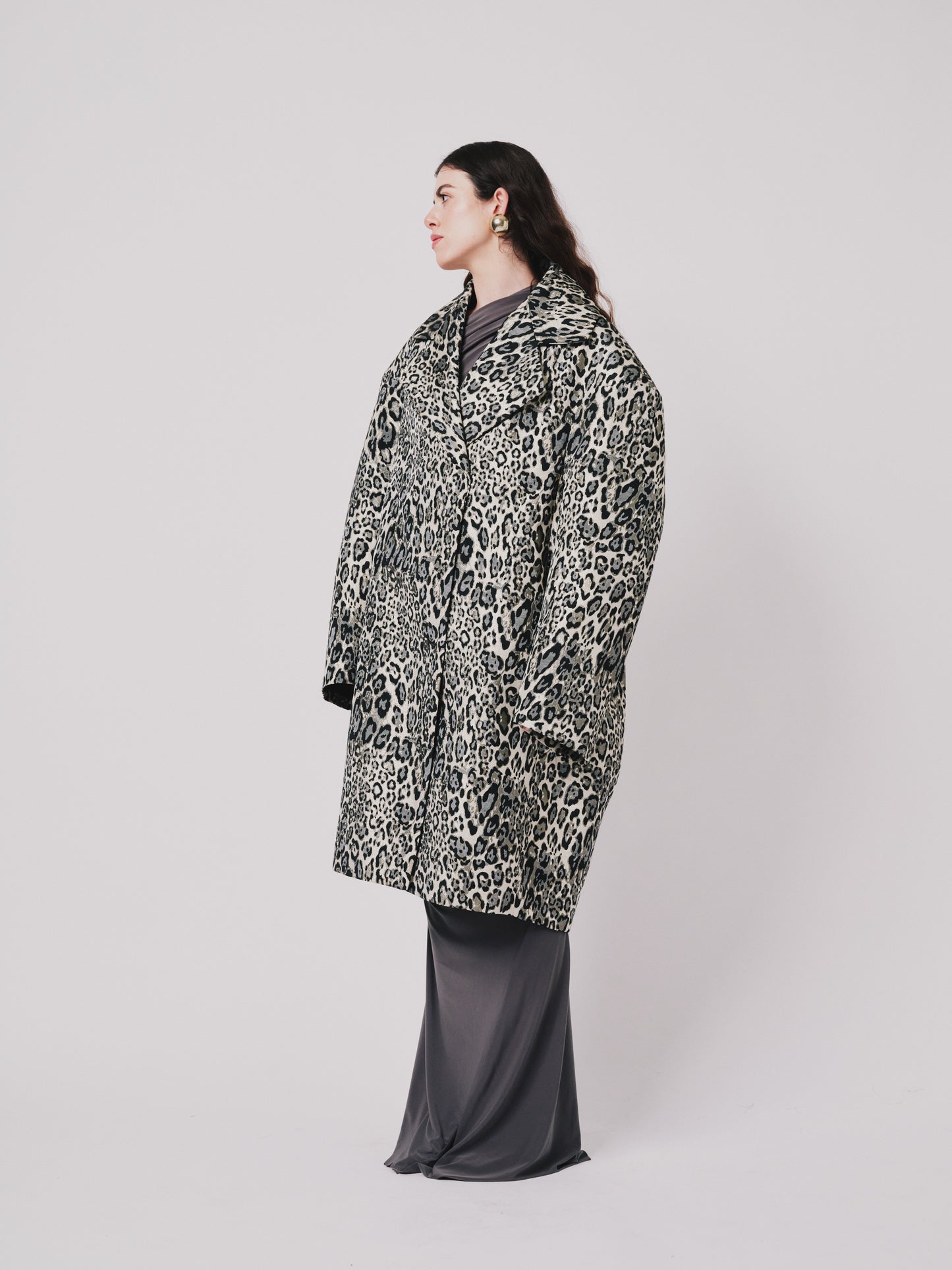 Person wearing a leopard print coat on a plain background side view 