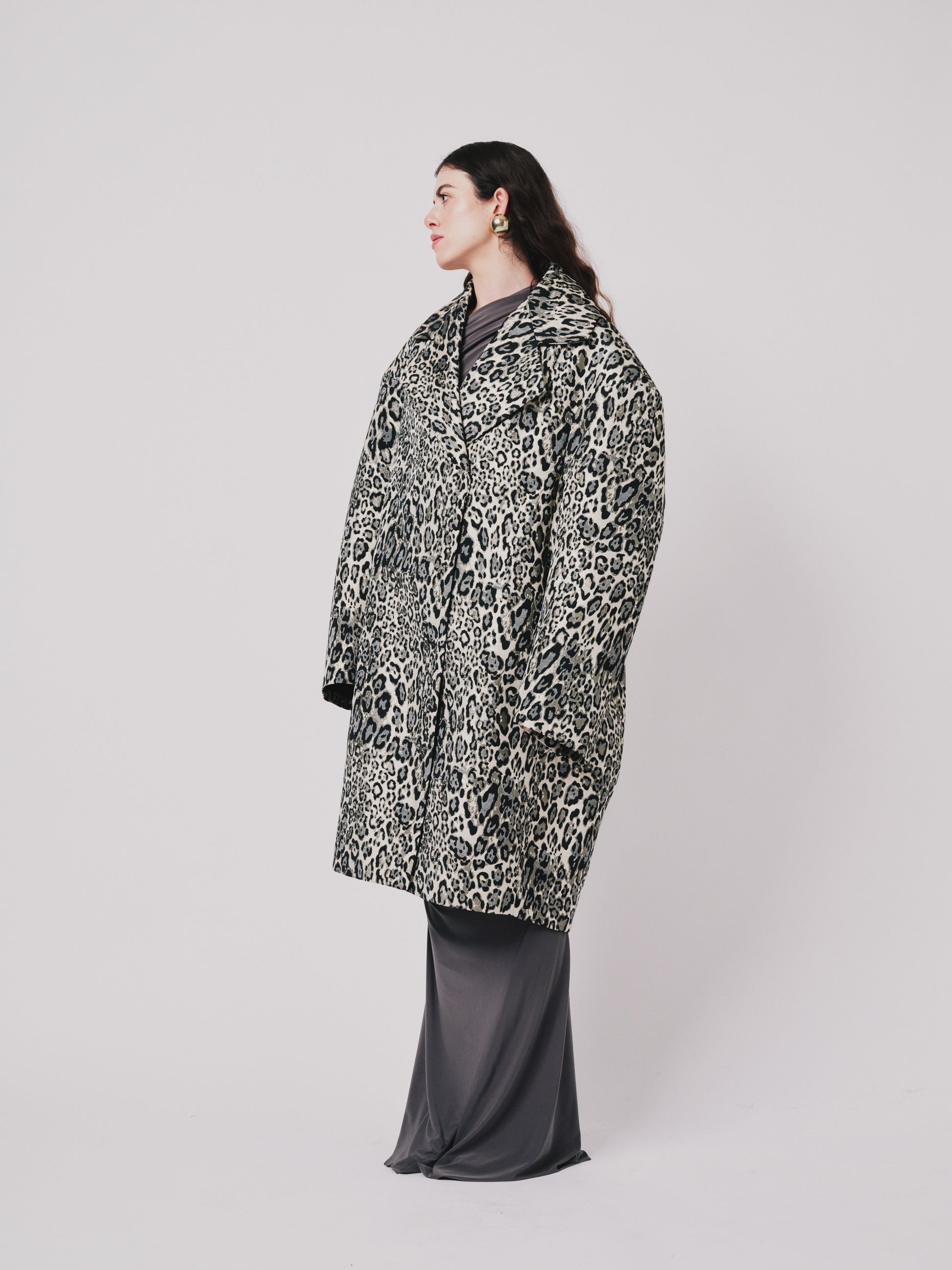 Person wearing a leopard print coat on a plain background side view 