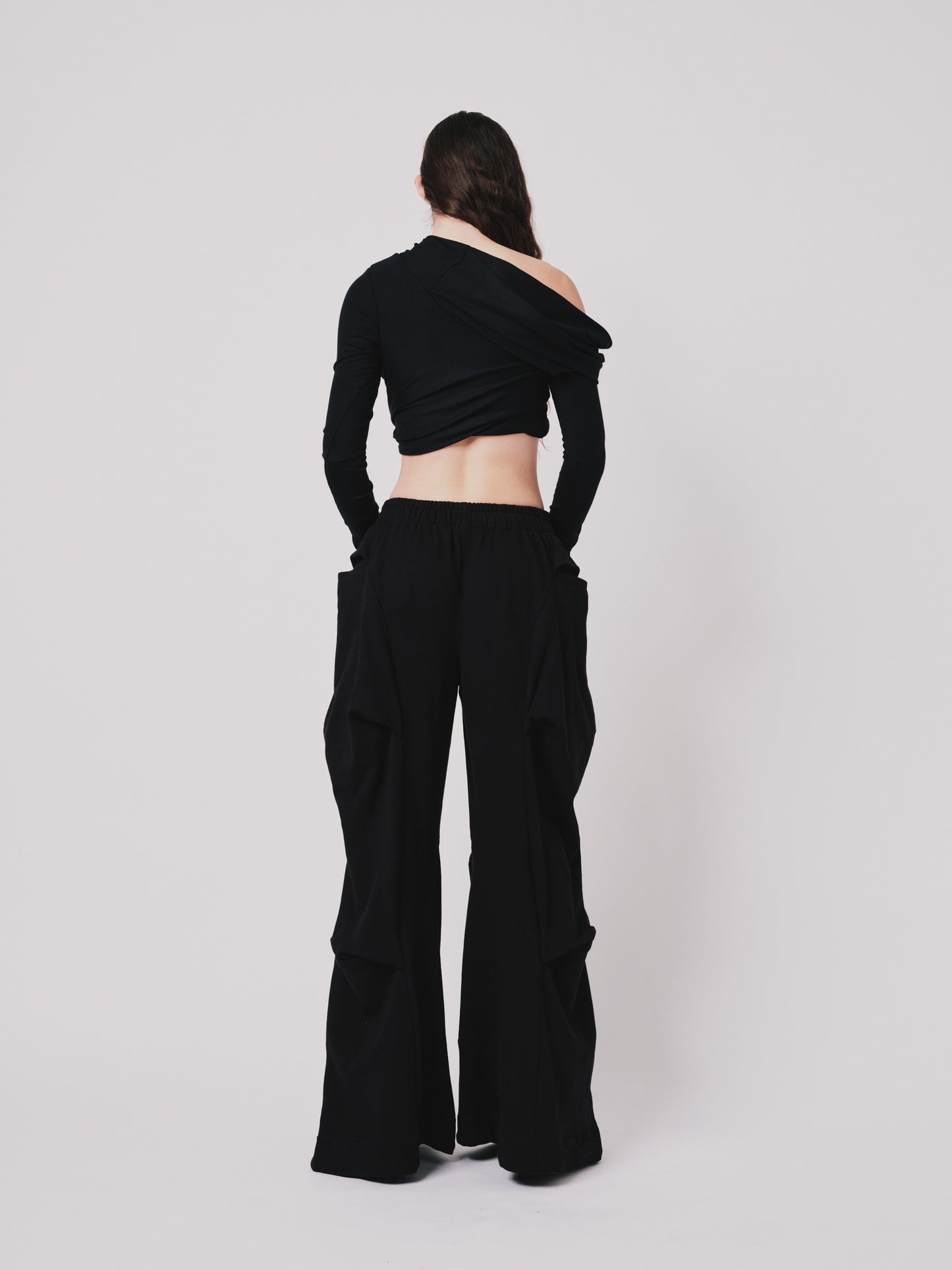 Woman wearing off the shoulder draped top. Cropped in black merino wool on white background. Back view