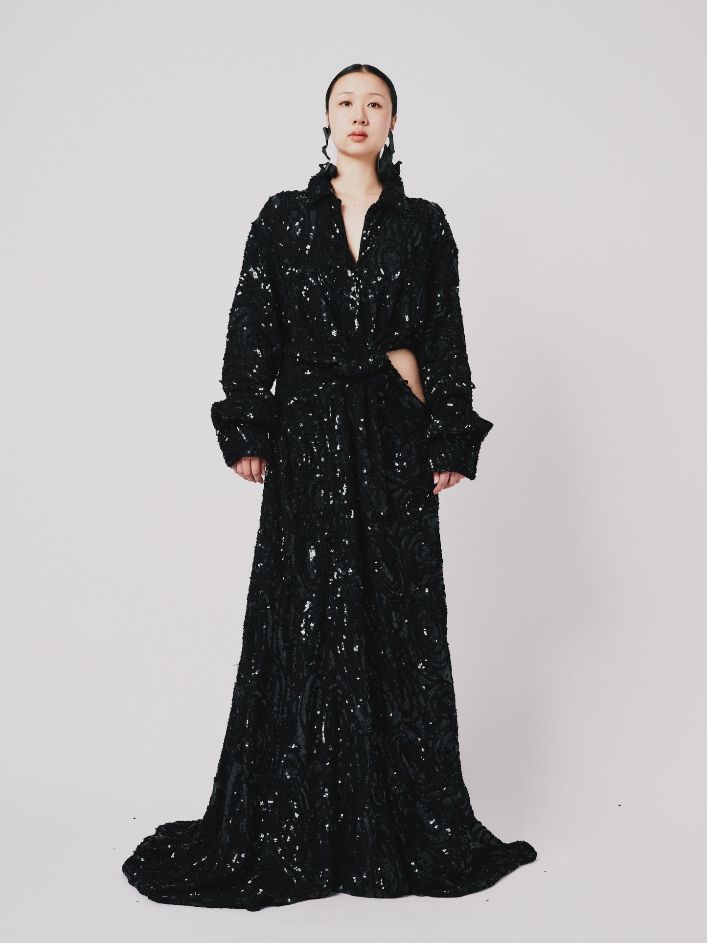 Woman wearing a black sequin Marq Twisted Draped dress against a white background. Front view