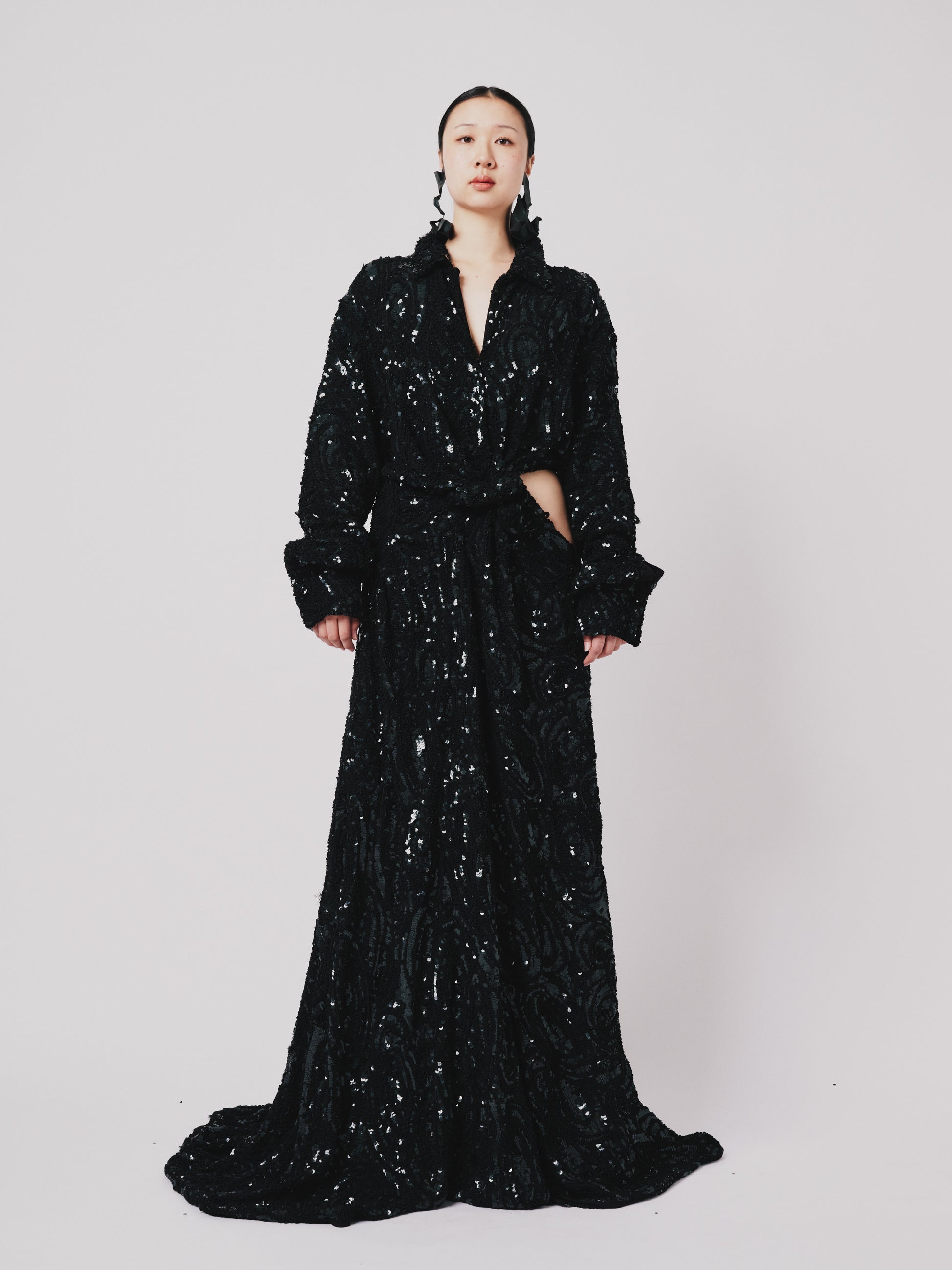 Woman wearing a black sequin Marq Twisted Draped dress against a white background. Front view