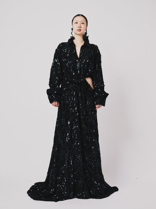 Woman wearing a black sequin Marq Twisted Draped dress against a white background. Front view