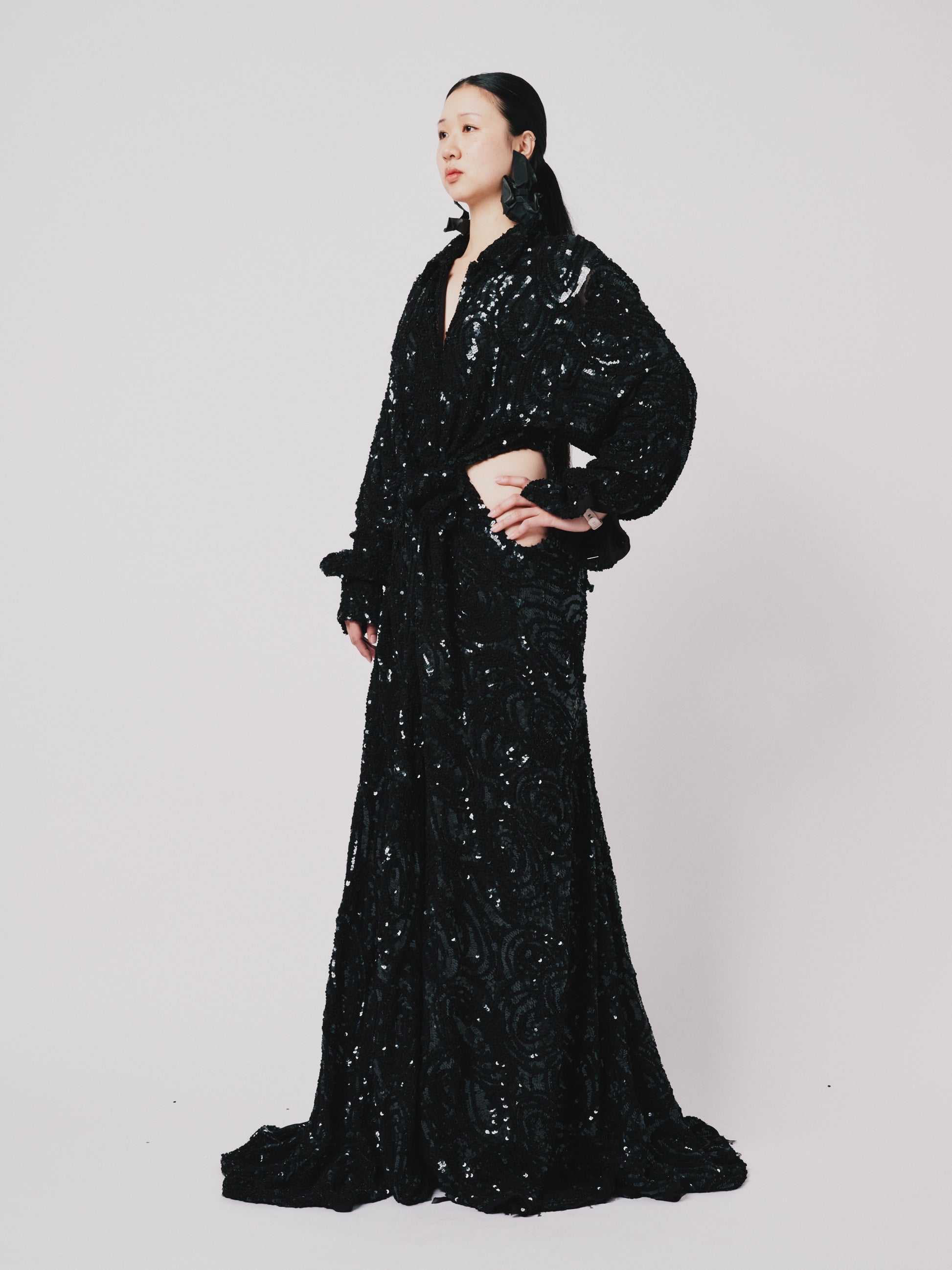 Person wearing a black sequin Marq twisted Draped dress against a white background. Side view