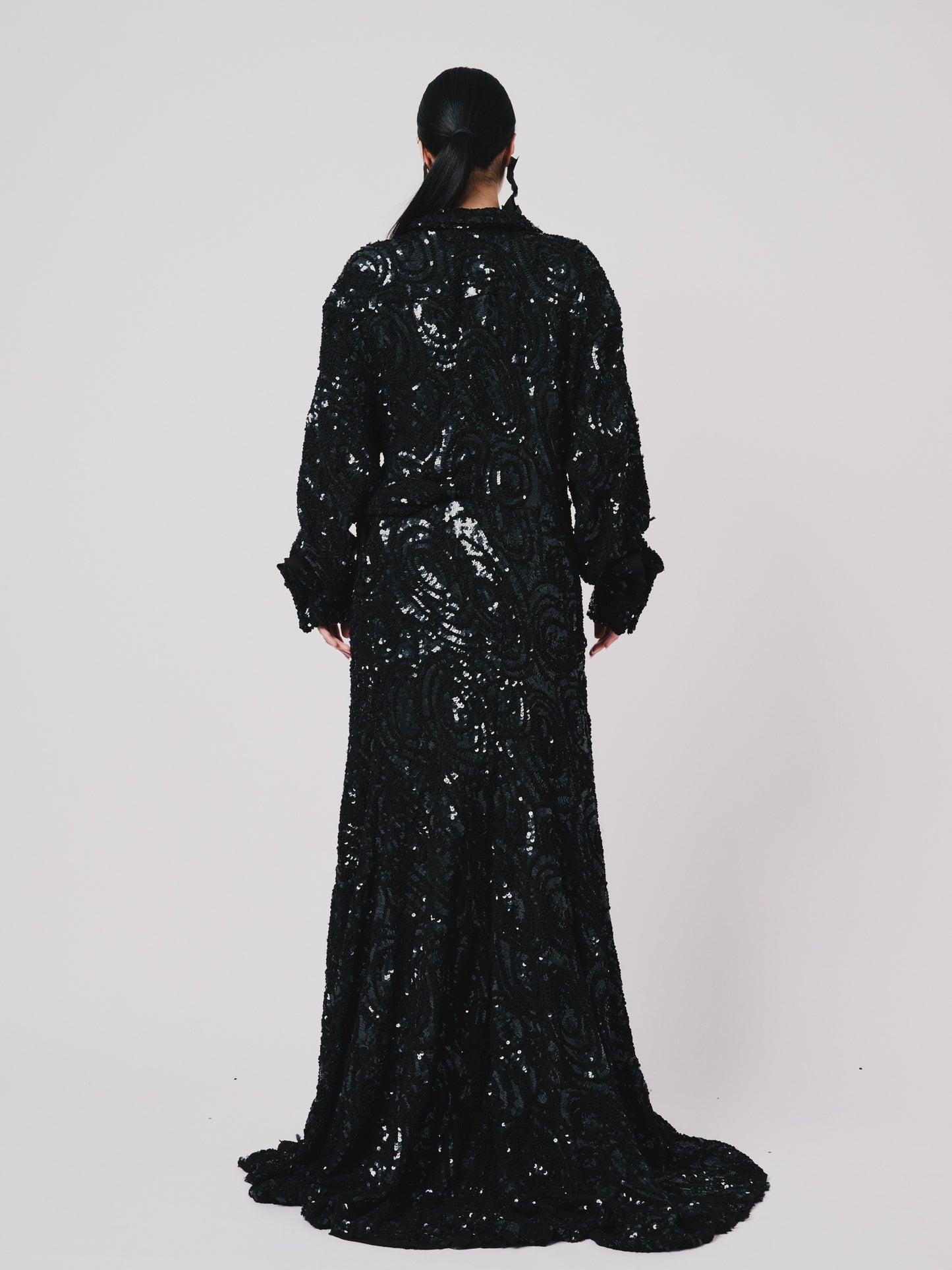 Person wearing a black sequin Marq twisted draped dress against a white background. Back view