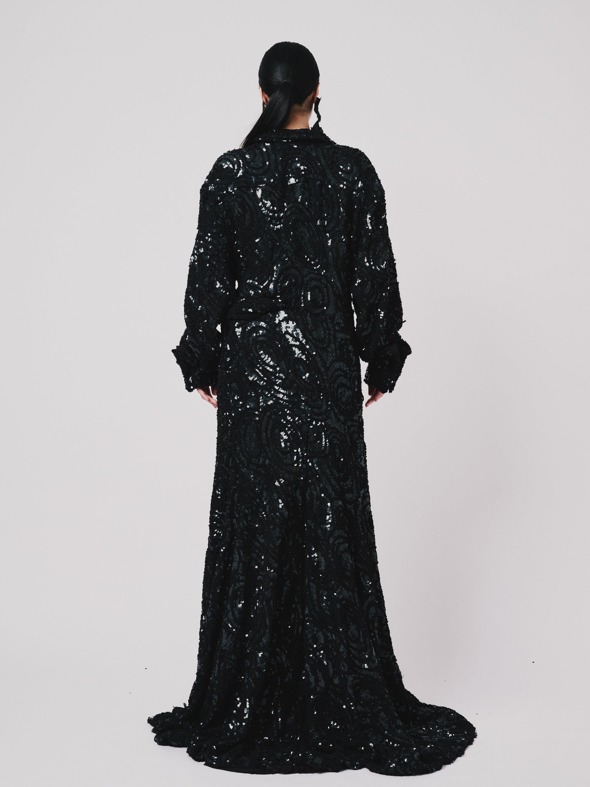 Person wearing a black sequin Marq twisted draped dress against a white background. Back view