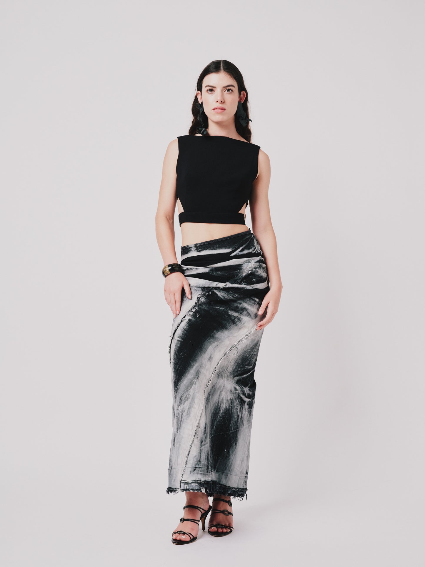 Woman wearing a structured drape skirt in distressed black denim on a plain background. Front view