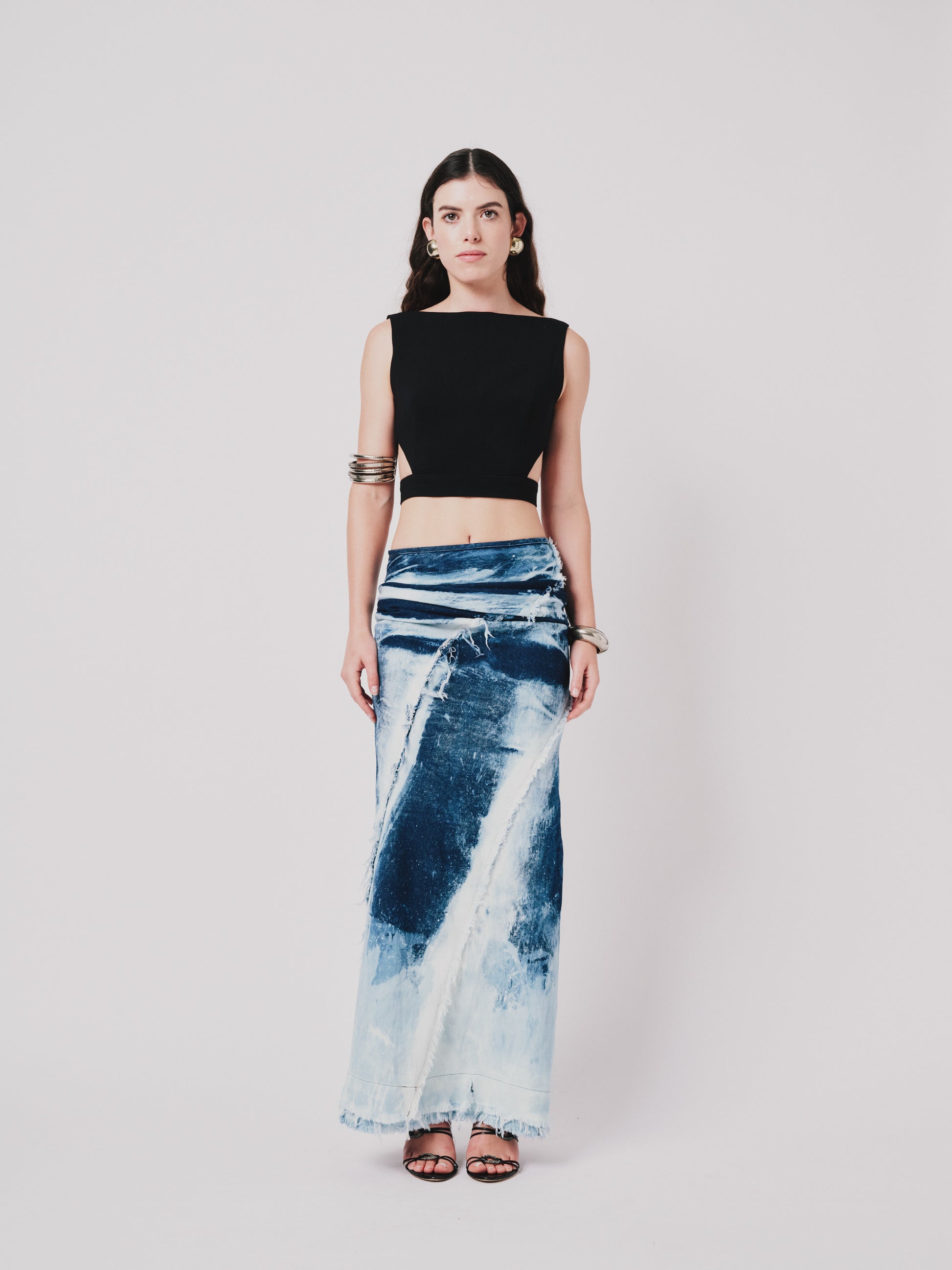 Woman wearing a black top and structured drape skirt in blue denim on a white background. Front view