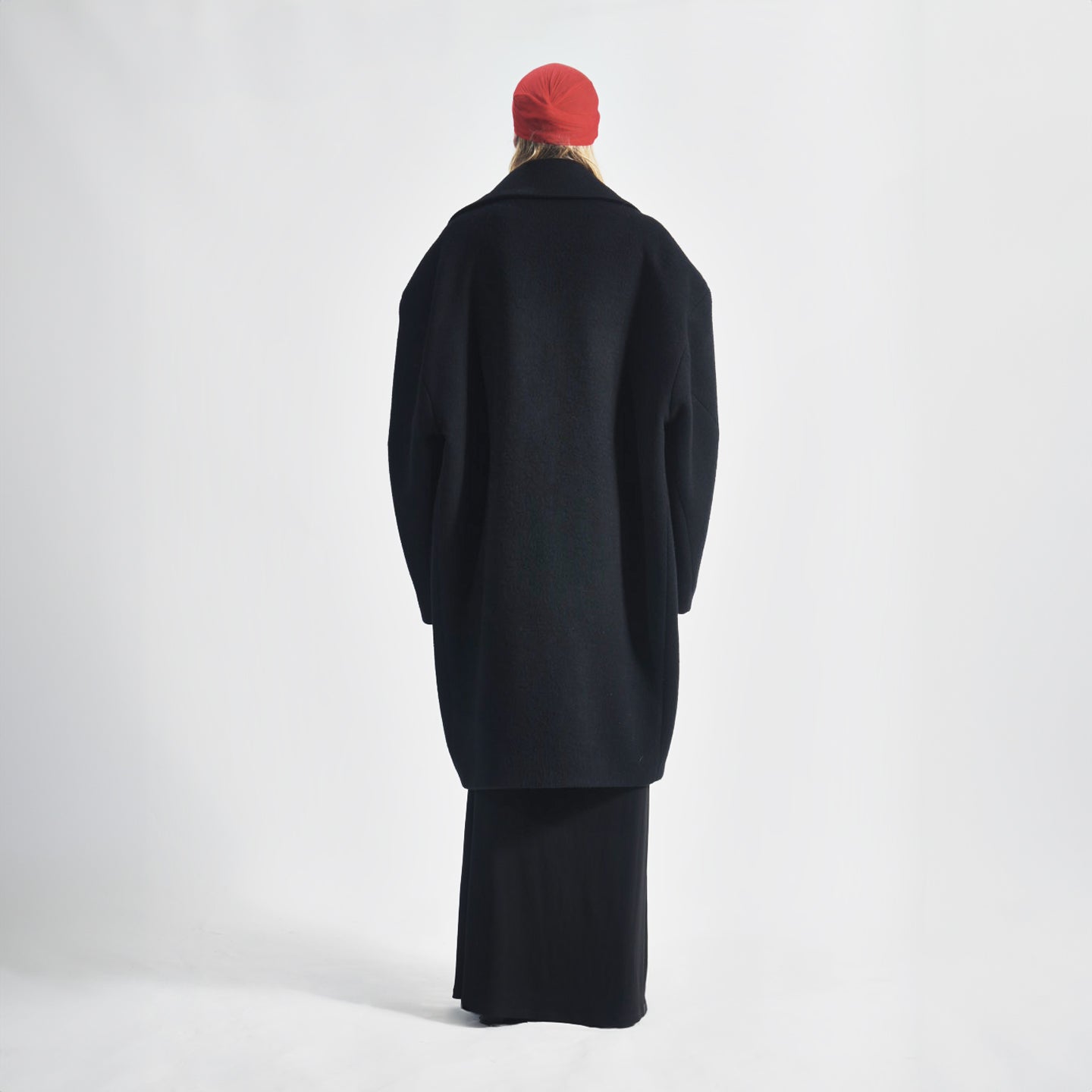 Back view of the black Hoffman Coat highlighting the unique cut sleeve with dart detail and over-the-knee length.